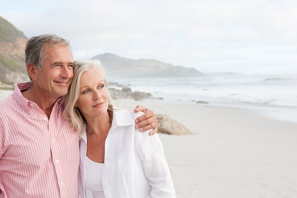 Older couple standing on a beach, facing the water.