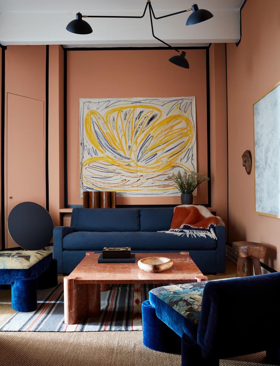 In the den, which is painted Dead Salmon from Farrow & Ball, with navy blue trim, a painting by Tamuna Sirbiladze (courtesy the artist and James Fuentes) hangs above a Restoration Hardware sofa with a Viso cashmere blanket. Marble coffee table by Gae Aulenti on a vintage Native American rug. Valle designed the tapestry chairs, and the painting at right is by Katherine Keltner. Speaker by Bang & Olufsen.