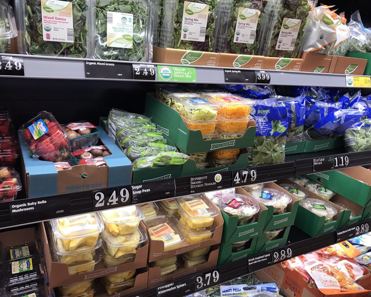 Closeup of 4 rows many different kinds of packaged vegetables in a refrigerated section of an aldi store, salads on the top row, spinach, green beans, and more, organized and clean