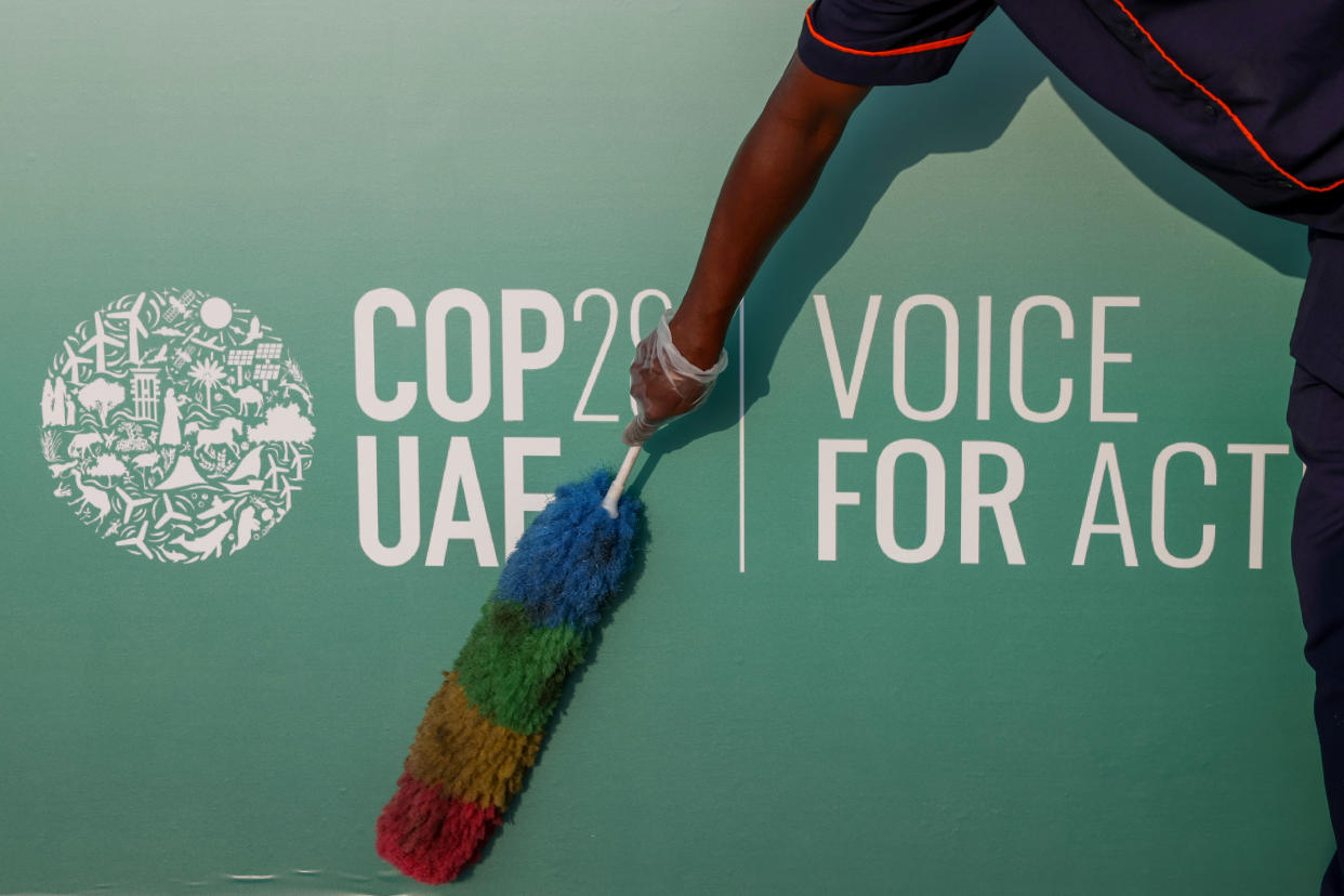 A worker dusts an event board for the COP28 climate conference.