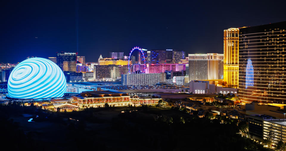 Las Vegas skyline at night featuring the illuminated MSG Sphere, casinos, resorts, and the High Roller Ferris wheel