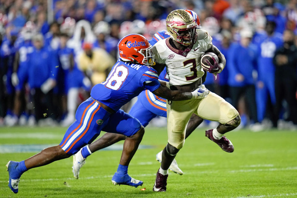 Florida State running back Trey Benson (3) slips past Florida safety Bryce Thornton (18) and safety Jordan Castell, back, on his way to a 26-yard touchdown during the second half of an NCAA college football game Saturday, Nov. 25, 2023, in Gainesville, Fla. (AP Photo/John Raoux)