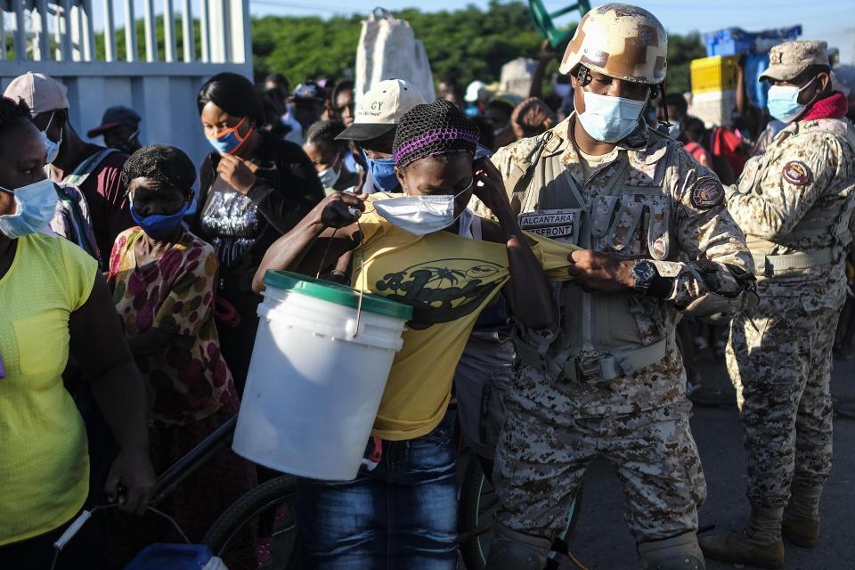 A woman, who is denied entry into the Dominican Republic, tries to put on her protective face mask as a soldier removes her from a line for not initially wearing the mask, at the border crossing in Dajabon, Dominican Republic, Friday, Nov. 19, 2021. An increasing mistreatment of the country’s Haitians, observers say, coincided with the rise of Luis Abinader, who took office as president in August 2020. (AP Photo/Matias Delacroix)