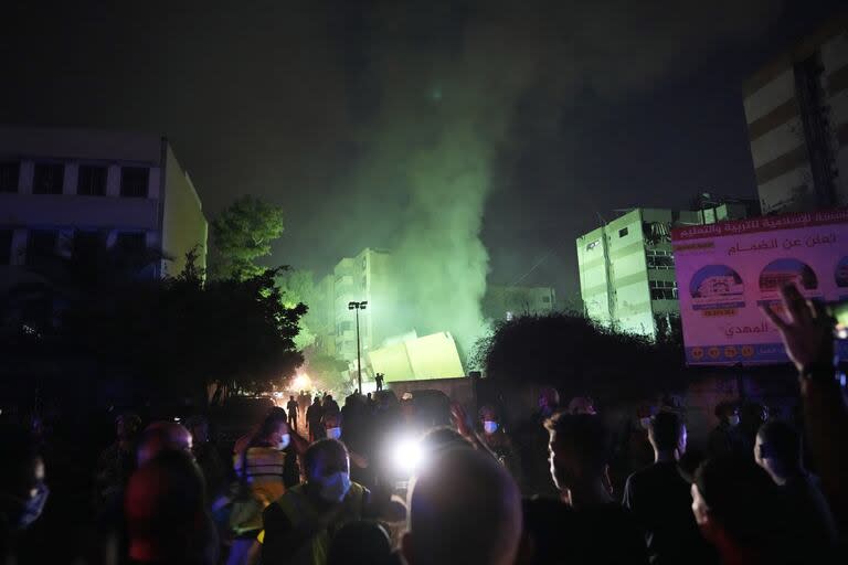 Varias personas se reúnen mientras sale humo de un edificio derrumbado en el lugar de un ataque aéreo israelí en los suburbios del sur de Beirut, el viernes 27 de septiembre de 2024.