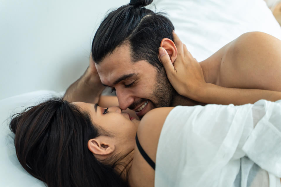 Caucasian man and Asian woman looking each other with happiness on bed. Attractive romantic sexy couple spend free leisure time, enjoy talking together after wake up in the morning in bedroom at home.