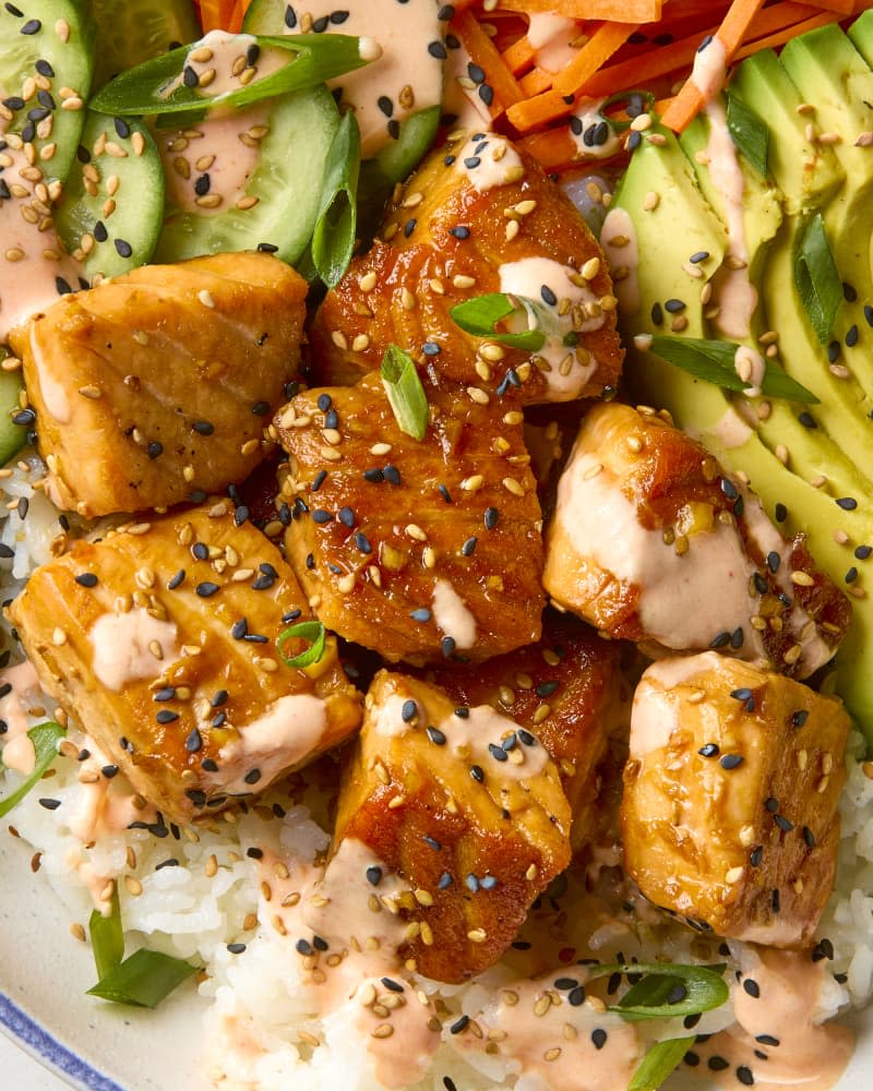 overhead shot of a salmon bowl with cucumbers, carrots and avocados, topped with black and white sesame seeds and spicy mayo