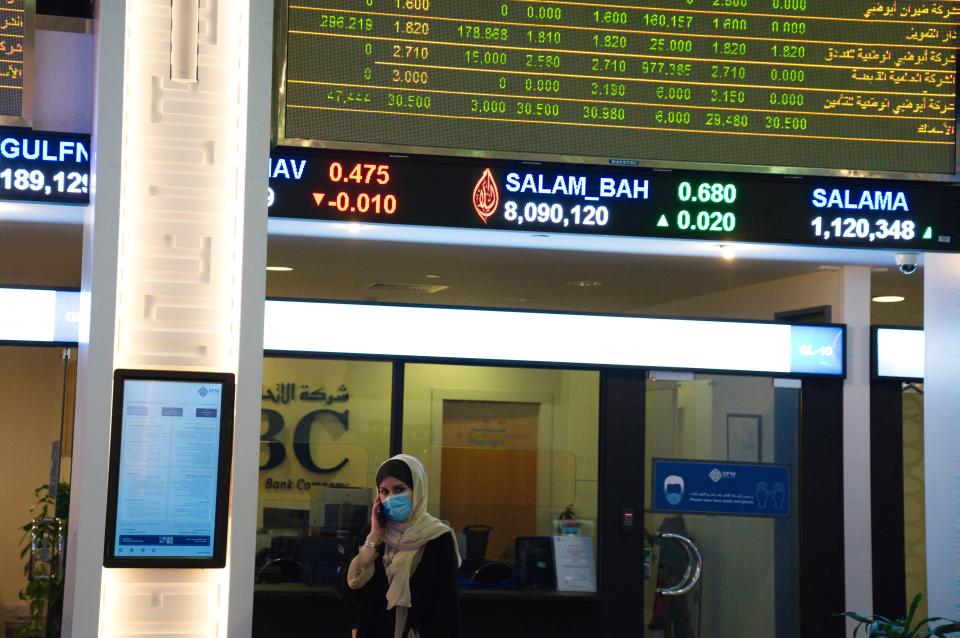 A woman wearing a face mask due to the coronavirus pandemic talks on the phone on the floor of the Dubai Financial Market in Dubai, United Arab Emirates, Tuesday, July 7, 2020. Dubai reopened its Dubai Financial Market stock exchange Tuesday after closing its floor due to the coronavirus pandemic. (AP Photo/Jon Gambrell)