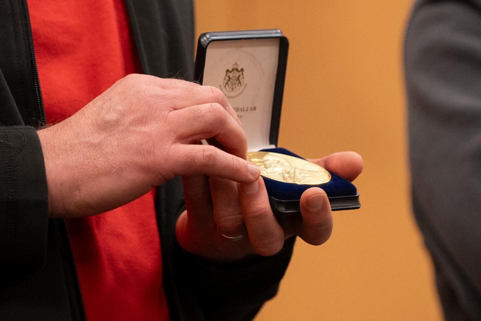 Michael Poirier, left, professor and chair of the Ohio State Department of Physics, holds a 24-karat gold replica of the 2023 Nobel Prize awarded to retired OSU faculty member and professor emeritus Pierre  Agostini on Wednesday at the OSU Physics Research Building. Agostini donated the replica to Ohio State to be displayed in the building. He and two other researchers won the Nobel Prize for experimental methods that generate attosecond pulses of light for the study of electron dynamics in matter.