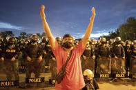 A protestor gestures as police stand guard near the Government House, during a demonstration in Bangkok, Thailand, Thursday, June 24, 2021. Pro-democracy demonstrators have taken to the streets of Thailand's capital again, marking the 89th anniversary of the overthrow of the country's absolute monarchy by renewing their demands that the government step down, the constitution be amended and the monarchy become more accountable. (AP Photo/Wason Wanichakorn)