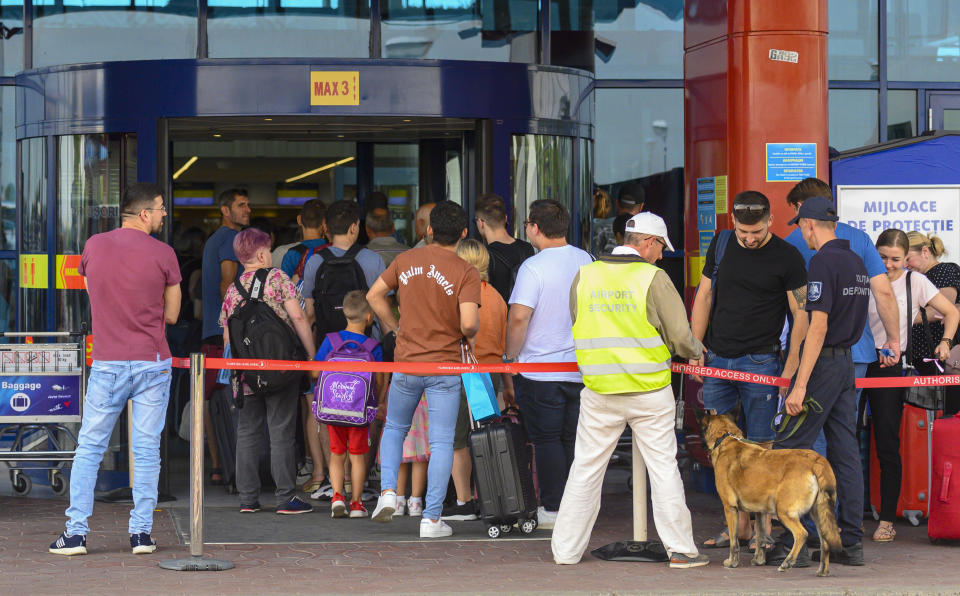 Security personnel and an explosive sniffing dog stand at the entrance of the departures terminal as passengers wait in line at the international airport in Chisinau, Moldova, Tuesday, Aug. 16, 2022. Over the last two months non-European Union Moldova, which shares a border with war-torn Ukraine, has been plagued by scores of bomb threats that have wreaked havoc on the resources of the already overstretched authorities.(AP Photo/Cristian Straista)