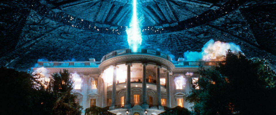 A scene from a film showing an alien spacecraft attacking a large building with a destructive beam