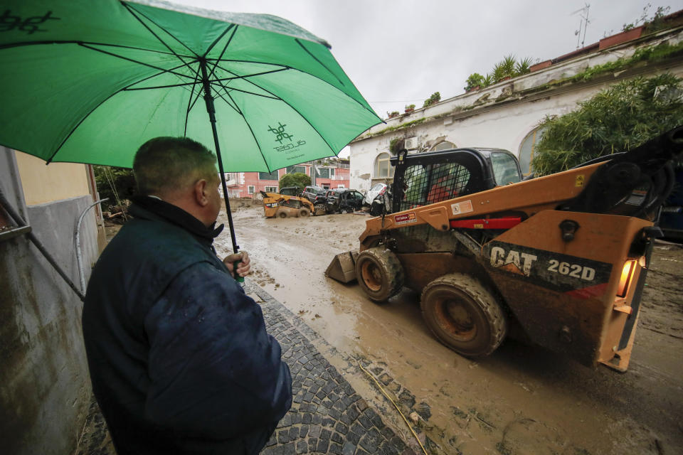 A man looks at a caterpillar as it removes mud from a street after heavy rainfall triggered landslides that collapsed buildings and left as many as 12 people missing, in Casamicciola, on the southern Italian island of Ischia, Saturday, Nov. 26, 2022. Firefighters are working on rescue efforts as reinforcements are being sent from nearby Naples, but are encountering difficulties in reaching the island either by motorboat or helicopter due to the weather. (AP Photo/Salvatore Laporta)