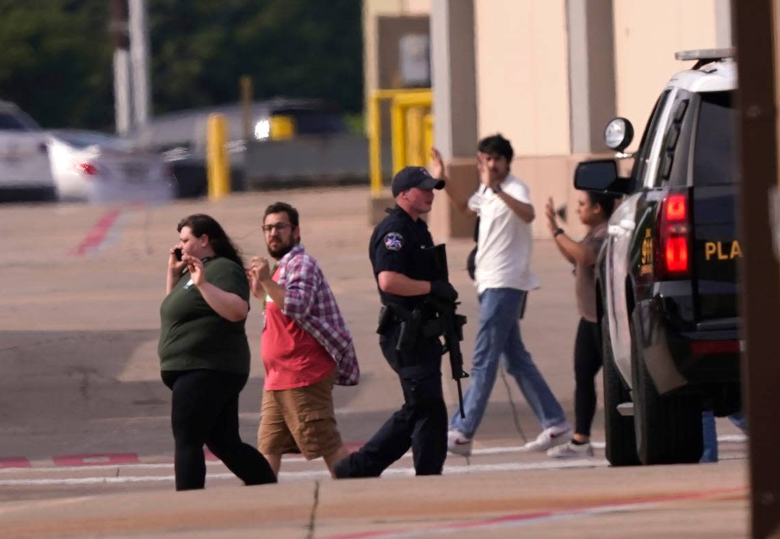 People raise their hands as they leave the Allen Premium Outlets following reports of a shooting on Saturday.