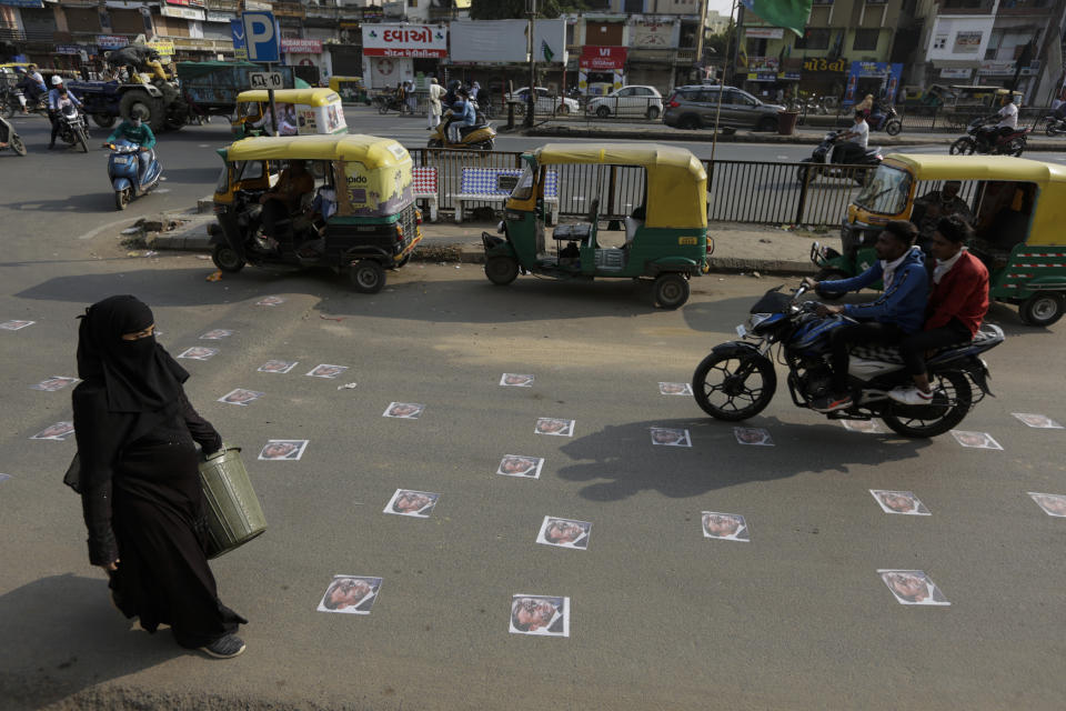 An Indian Muslim woman walks as commuters move on defaced images of French President Emmanuel Macron pasted by protestors on a road in Ahmedabad, India, Sunday, Nov. 1, 2020. Muslims have been calling for both protests and a boycott of French goods in response to France's stance on caricatures of Islam's most revered prophet. (AP Photo/Ajit Solanki)