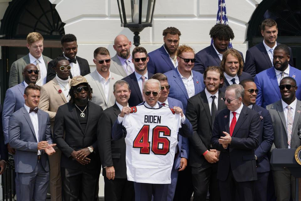 President Joe Biden, surrounded by members of the Tampa Bay Buccaneers, poses for a photo holding a jersey during a ceremony on the South Lawn of the White House, in Washington, Tuesday, July 20, 2021, where Biden honored the Super Bowl Champion Tampa Bay Buccaneers for their Super Bowl LV victory. (AP Photo/Andrew Harnik)