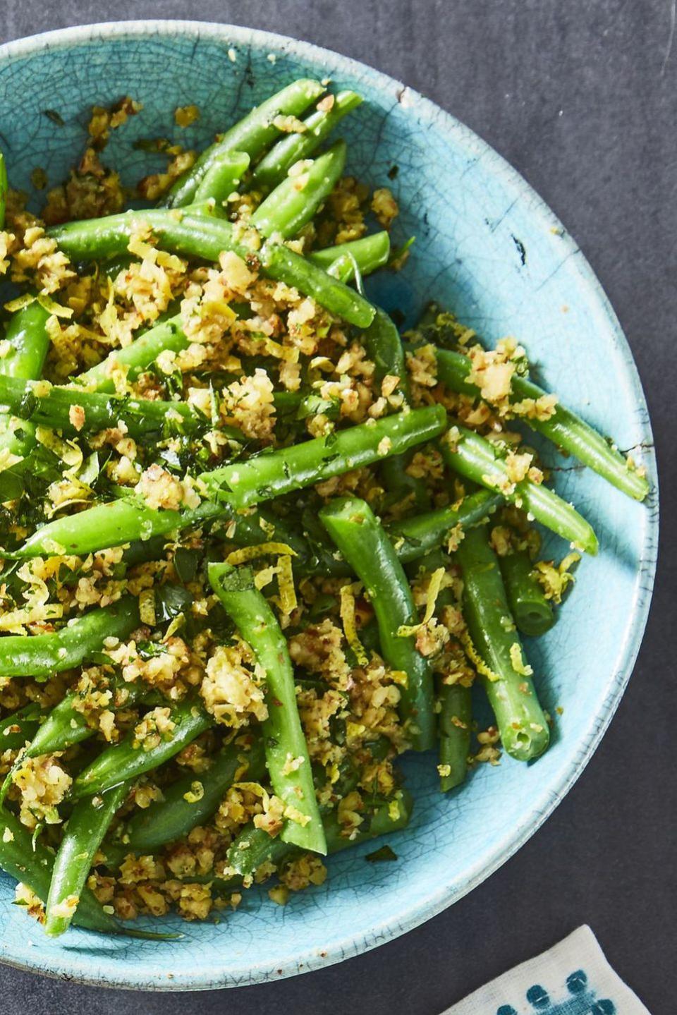 a close up of green beans with olive almond tapenade in a blue bowl