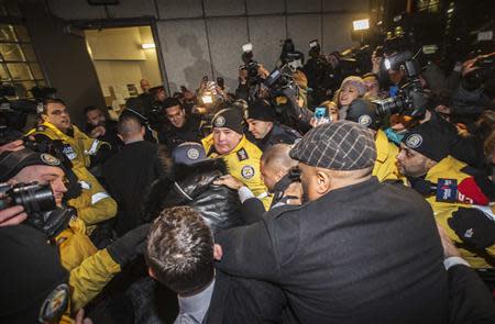 Pop singer Justin Bieber (C, cap) makes his way through a line of police officers upon arriving at a police station in Toronto January 29, 2014. REUTERS/Mark Blinch