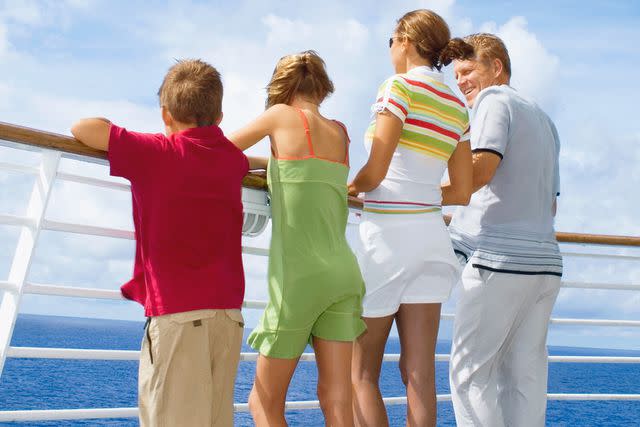 <p>David Sacks/Getty</p> Family standing on the deck of a cruise ship