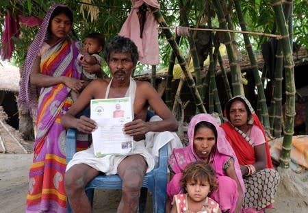 Nand Lal Mandhji, holds a letter about the Ayushman Bharat Medical Scheme, known as 'Modicare' as he sits outside his home with his family in Marwan village