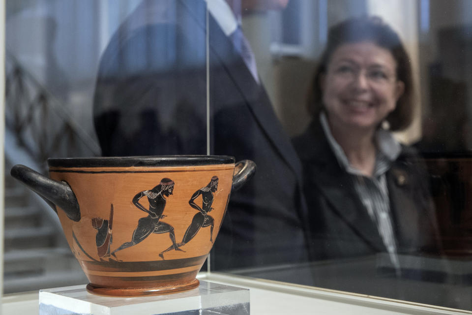 Greek Culture Minister Lina Mendoni stands behind an ancient Greek drinking cup decorated with runners, which was one of the awards presented to Spyros Louis, the Greek winner of the Marathon in the 1896 first modern Olympic Games, at the National Archaeological Museum in Athens on Wednesday, Nov. 13, 2019. Greece's Culture Ministry said Wednesday the ancient vase has been returned to Athens by the University of Muenster in Germany where it had ended up.(AP Photo/Petros Giannakouris)