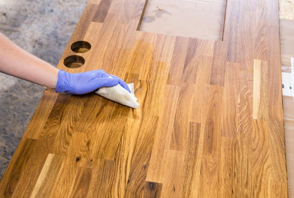 Gloved hand applying a linseed oil finish to a butcher block countertop before installation