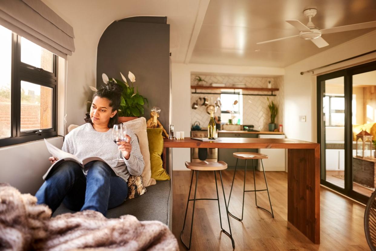 Woman holding a glass of wine and reading a magazine while relaxing on the couch at home