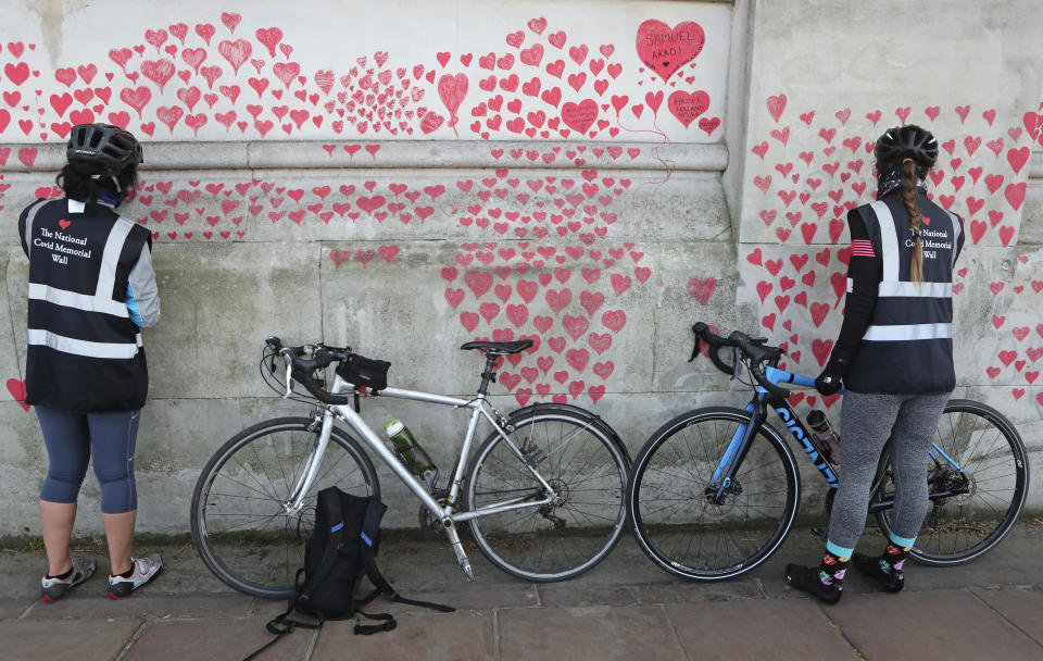 Women draw hearts on the 'The National COVID Memorial Wall' on the south bank of the Thames in front of St. Thomas' hospital and opposite the House of Parliament in London, Sunday April 4, 2021. Hearts are being drawn onto the wall in memory of the many thousands of people who have died in the UK from coronavirus, with organizers hoping to reach their target of 150,000 hearts by the middle of next week. (AP Photo/Tony Hicks)