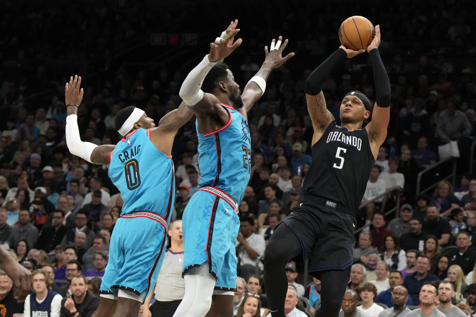 Orlando Magic forward Paolo Banchero shoots over Phoenix Suns forward Torrey Craig and center Deandre Ayton (22) during the first half of an NBA basketball game, Thursday, March 16, 2023, in Phoenix. (AP Photo/Rick Scuteri)