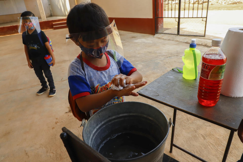 Wearing a mask and face shield to curb the spread of the new coronavirus, a student washes his hands before entering for his first day of class at the Valentin Gomez Farias Indigenous Primary School in Montebello, Hecelchakan, Campeche state, Monday, April 19, 2021. Campeche is the first state to transition back to the classroom after a year of remote learning due to the pandemic. (AP Photo/Martin Zetina)