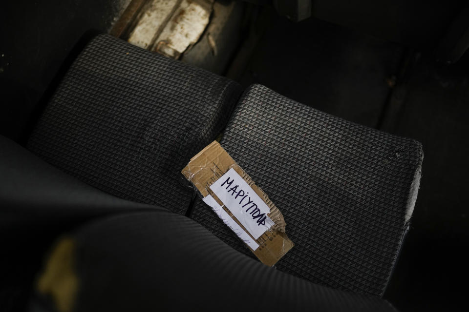 A handwritten sign that reads in Ukrainian: "Mariupol" lies on a seat in a minibus used to evacuate people from Mariupol in a reception center for displaced people in Zaporizhzhia, Ukraine, Sunday, May 8, 2022. Volunteer drivers are risking everything to deliver humanitarian aid to Ukrainians behind the front lines of the war — and to help many of them escape. The routes are dangerous and long and the drivers risk detention, injury or death. (AP Photo/Francisco Seco)