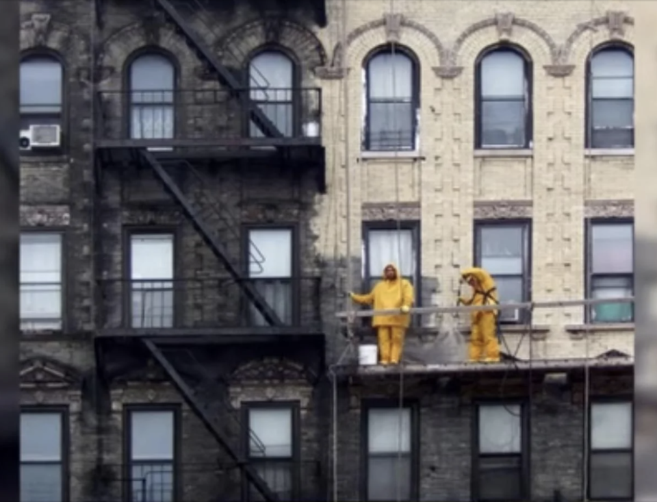 Two individuals in yellow raincoats on a building's fire escape