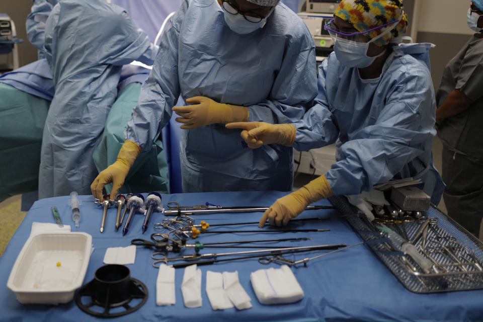 Medical assistants prepare surgical instruments for surgeon Lara Ribeiro Parenti during the surgery of Caroline Erganian at Bichat Hospital, AP-HP, in Paris, Wednesday, Dec. 2, 2020. Erganian, 58, hopes to shed more than a third of her weight as a result of having a large part of her stomach cut out and be free of knee and back pain — and of her cane. She prayed in the final weeks that her phone wouldn't ring with news of another delay. (AP Photo/Francois Mori)