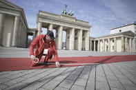 A man fastens the red carpet in front of the Brandenburg Gate in Berlin, Germany, ahead of British King Charles III's visit to Germany, Wednesday, March 29, 2023. Before his coronation in May 2023, the British king and his royal wife will visit Germany for three days. (Michael Kappeler/dpa via AP)