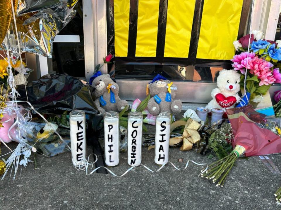 Four candles, labeled "Keke," "Phil," "Corbin" and "Siah" stand in front of a doorway surrounded by flowers, stuffed animals and balloons.