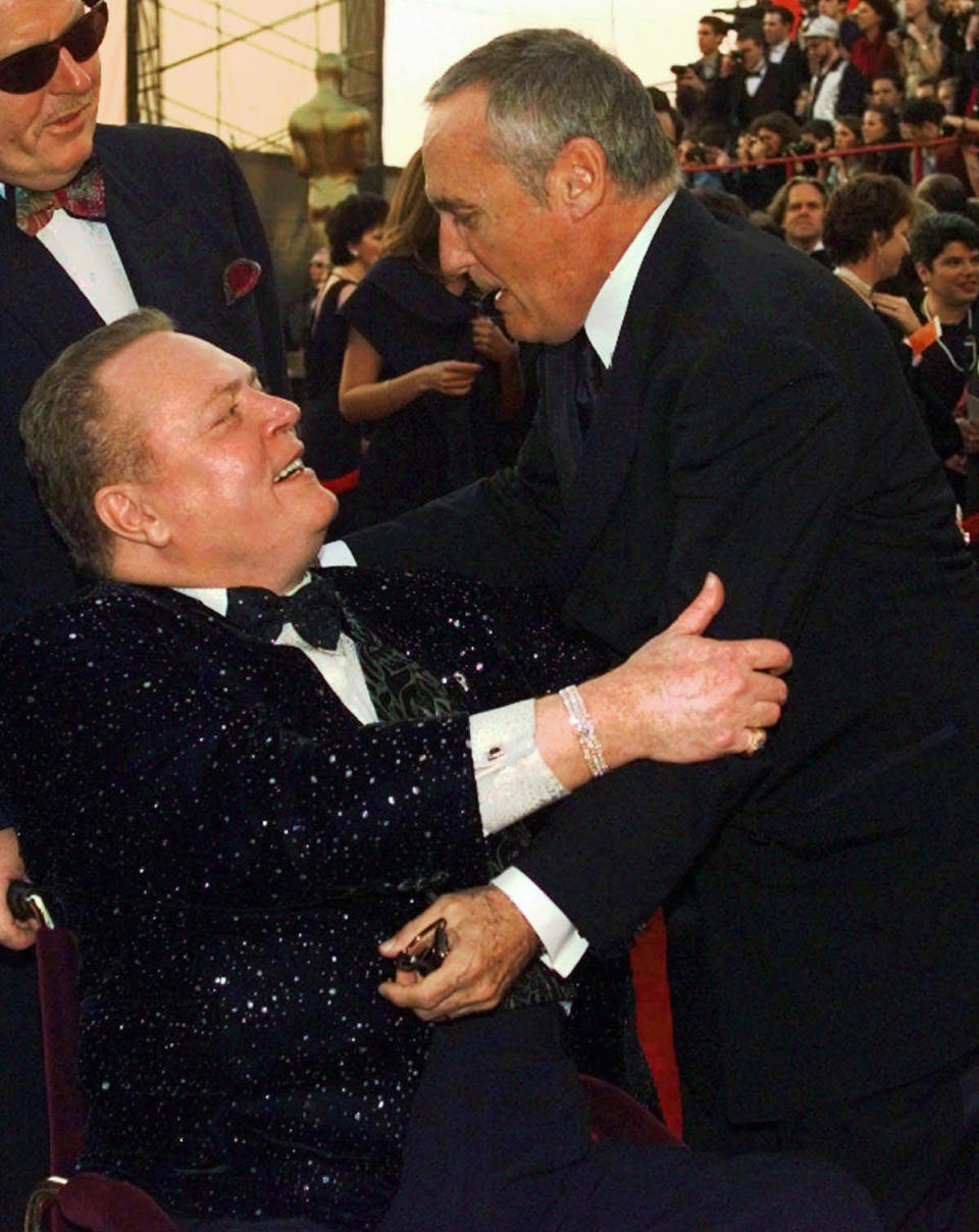 FILE - Dennis Hopper, right, gives Larry Flynt a hug as they arrive for the 69th Annual Academy Awards on March 24, 1997, in Los Angeles. Flynt, who turned "Hustler" magazine into an adult entertainment empire while championing First Amendment rights, has died at age 78. His nephew, Jimmy Flynt Jr., told The Associated Press that Flynt died Wednesday, Feb. 10, 2021, of heart failure at his Hollywood Hills home in Los Angeles. (AP Photo/Michael Caulfield, File)