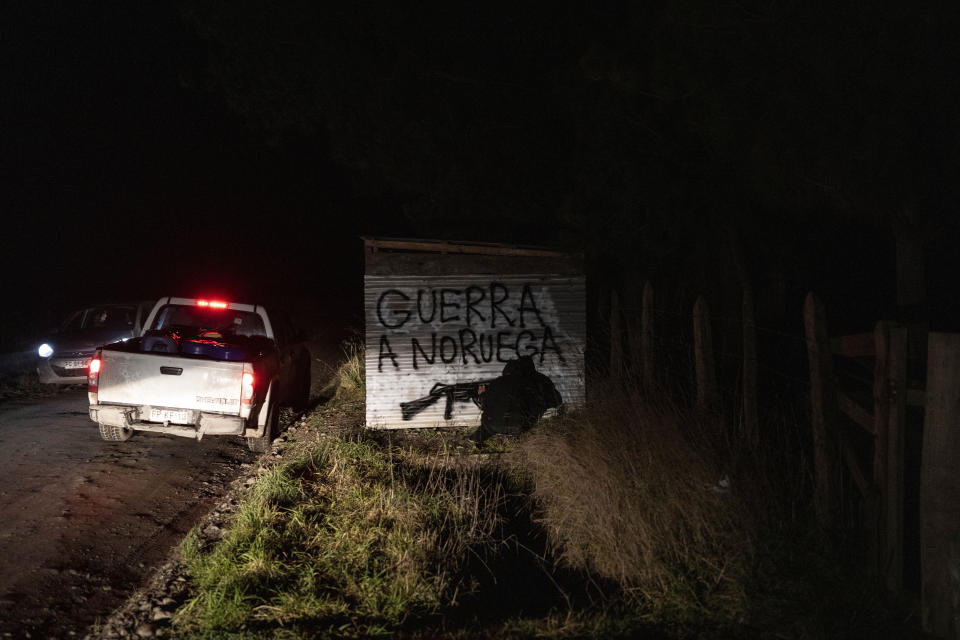 A Mapuche man spray-paints a weapon under a message reading "War with Norway," in Spanish, on the side of a bus stop near the entrance to a hydroelectric plant construction site owned by the Norwegian company Statkraft in Carimallin, southern Chile, on Saturday, June 25, 2022. In September Chileans will vote on a new and controversial constitution spotlighting Indigenous rights and land restitution. (AP Photo/Rodrigo Abd)