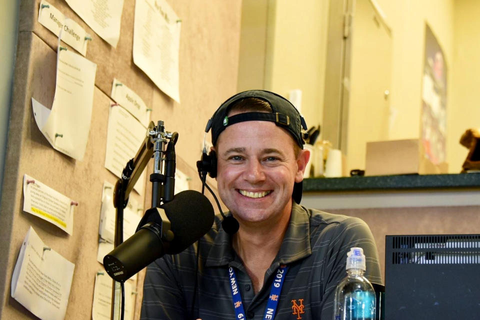 In this Sept 11, 2019, photo provided by Colin Cosell, Colin Cosell smiles inside the public address booth during a baseball game between the New York Mets and the Arizona Diamondbacks at Citi Field in New York. The public address announcer for the New York Mets is trying to cheer fans one at a time, recording personalized messages for them, echoing the booming introductions big league hitters get when they step up to home plate. (MJ Lupton via AP)