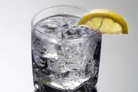 Club soda or Vodka / Gin and tonic mixed drink with lemon slice on a gray background with reflection