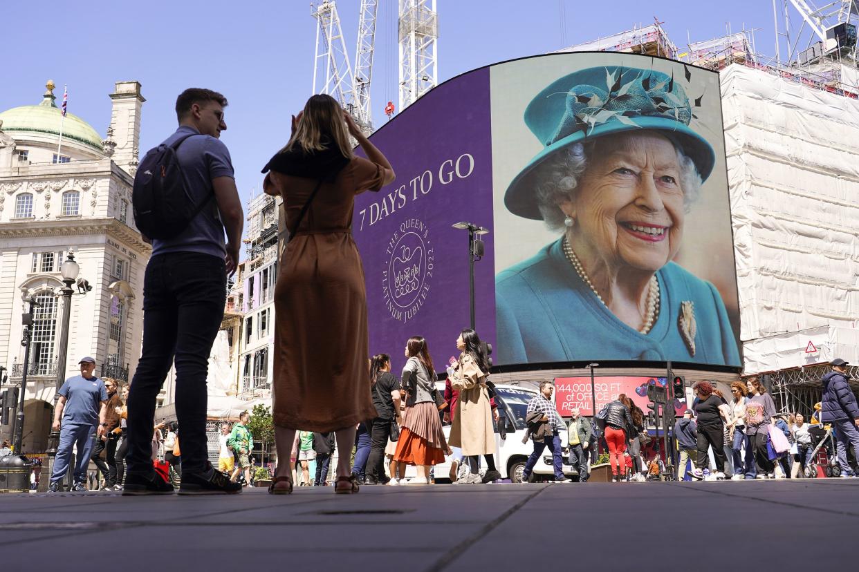 People walk past the screen in Piccadilly Circus as it displays a 7-day countdown to the Queen's Platinum Jubilee, featuring two photos of Britain's Queen Elizabeth, in London on Friday, May 27, 2022.