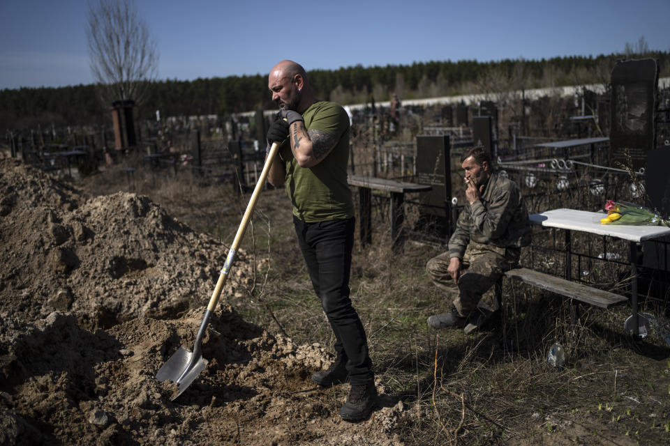Cemetery worker Vladislav, left, takes a break from working at the funeral of Tetyana Gramushnyak, 75, killed by shelling on March 19 while cooking food outside her home in Bucha, in the outskirts of Kyiv, Ukraine, Thursday April 14, 2022. (AP Photo/Rodrigo Abd)