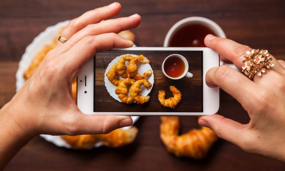 Taking a photograph with cell phone of breakfast made of one cup of black tea and six croissants.