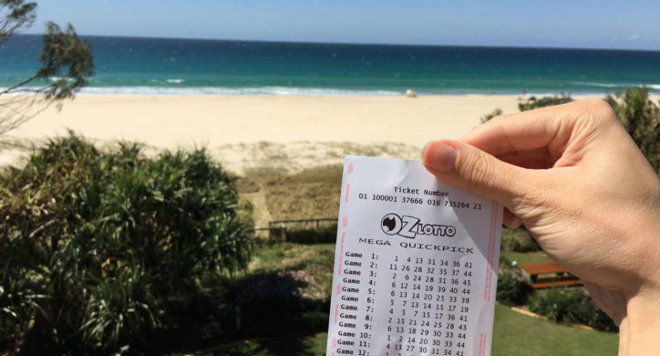 Stock photo of an OzLotto ticket held in front of a beach. Source: The Lott