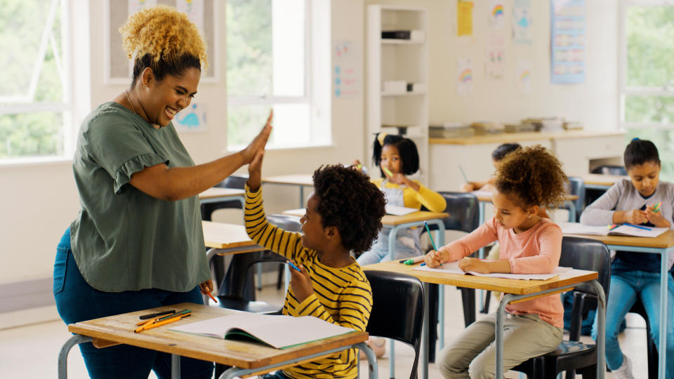 Teacher high fiving a student sitting at a desk