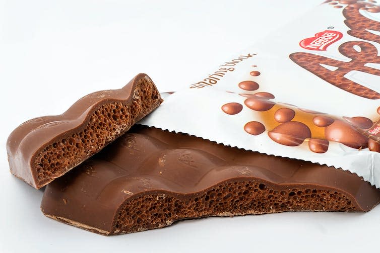 A macro close-up shot of an opened bar of Aero chocolate, with the corner broken off, exposing the unique bubble texture from which it gets it name.