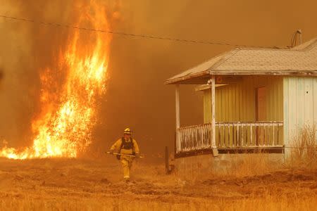 A firefighter walks near a home as flames from the fast-moving Detwiler fire approach in Mariposa, California U.S. July 19, 2017. REUTERS/Stephen Lam