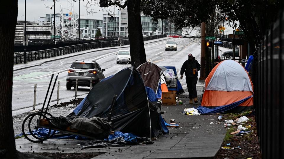 PHOTO: In this Jan. 24, 2024 file photo, a pedestrian walks past an encampment of tents after crossing Hoyt Street in Portland, Ore. (Patrick T. Fallon/AFP via Getty Images, FILE)