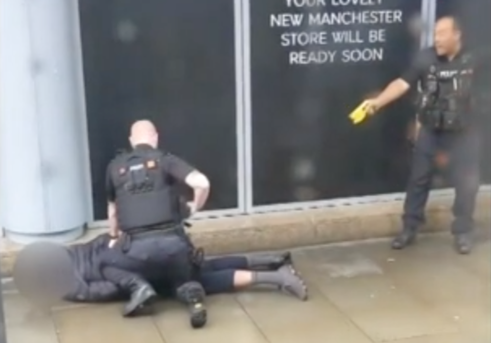 An officer points a Taser at a man held down on the floor by a second police officer outside the Arndale shopping centre in Salford, Manchester (TWITTER/JohnGreenhalgh)