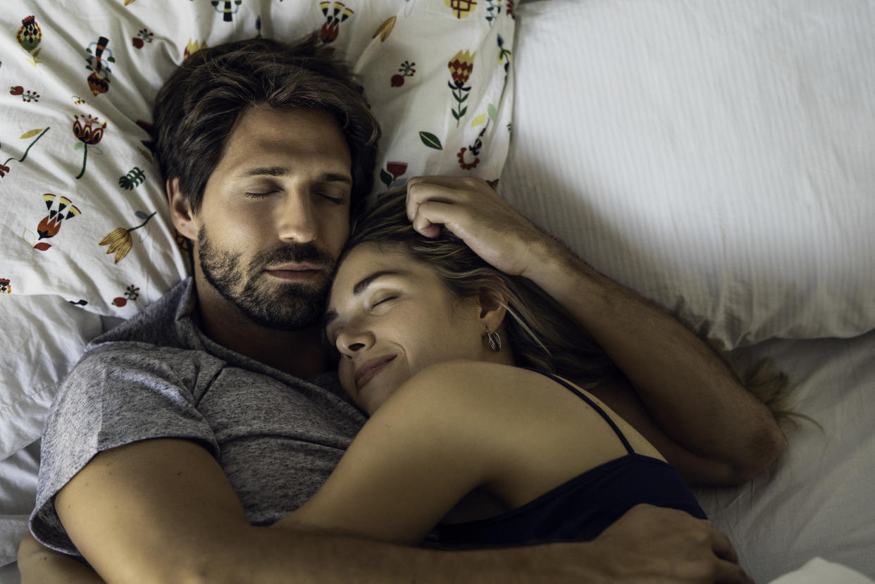 Overhead view of young couple hugging while sleeping on bed in bedroom