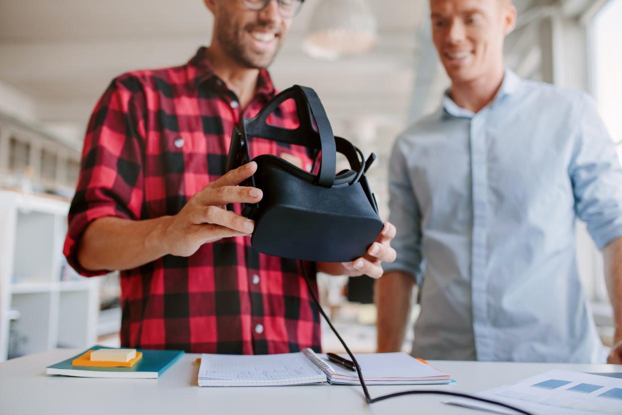 Shot of two men using virtual reality goggles in office. Business partners working in office, standing at a table with VR glasses.