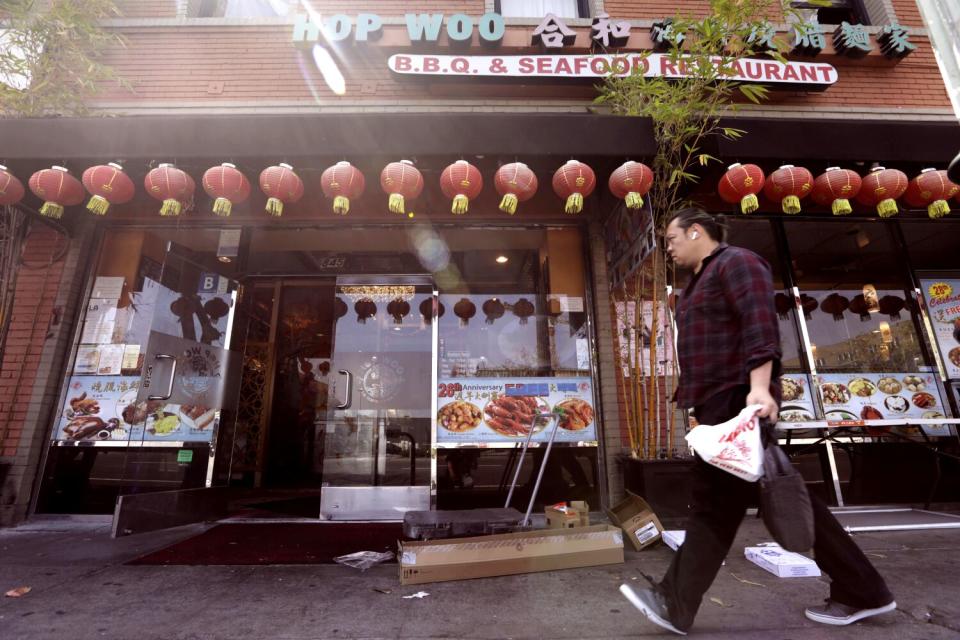 An exterior of the red-lantern-adorned exterior of Hop Woo. A man walks past the camera.